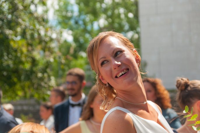 Femme souriante en robe de mariée, entourée de convives lors d'un mariage en extérieur.