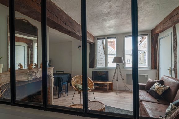 Salon moderne avec un canapé, télévision et lumière naturelle à travers de grandes fenêtres.