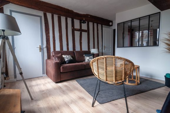 Salon cosy avec un canapé marron, une chaise en rotin et un sol en parquet.