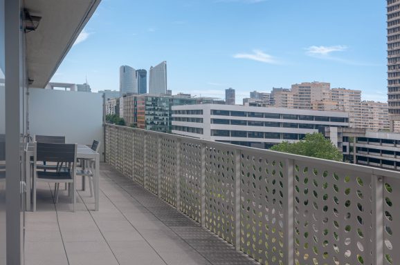 Vue d'un balcon avec une balustrade, surplombant des immeubles modernes.