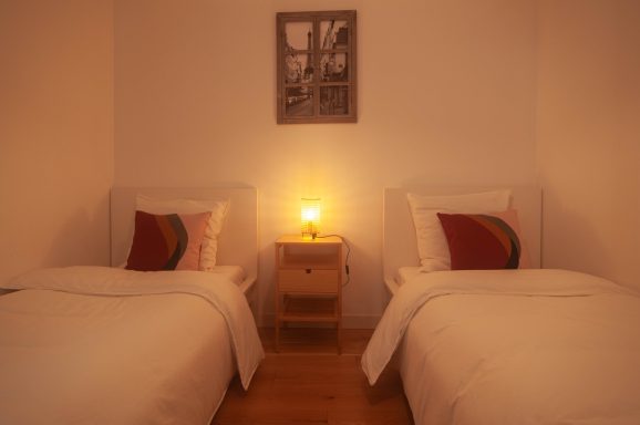 Chambre lumineuse avec deux lits simples et une table de nuit éclairée.