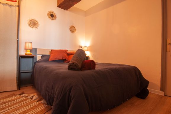 Chambre cosy avec lit double, draps sombres et accessoires décoratifs.