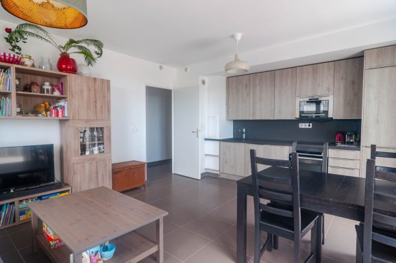 Salon moderne avec cuisine ouverte, meubles en bois et décoration colorée.
